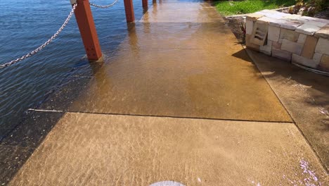 Un-Cartel-De-Basura-Para-Perros,-Bajo-El-Agua-En-Una-Pasarela-Se-Eleva-Hasta-Una-Vista-De-Un-Suburbio-Australiano-Frente-Al-Mar