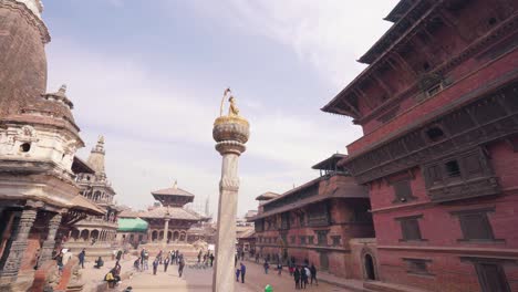 view of king yoganarendra malla bronze statue over stone column with people walking in patan durbar square. kathmandu, nepal - timelapse