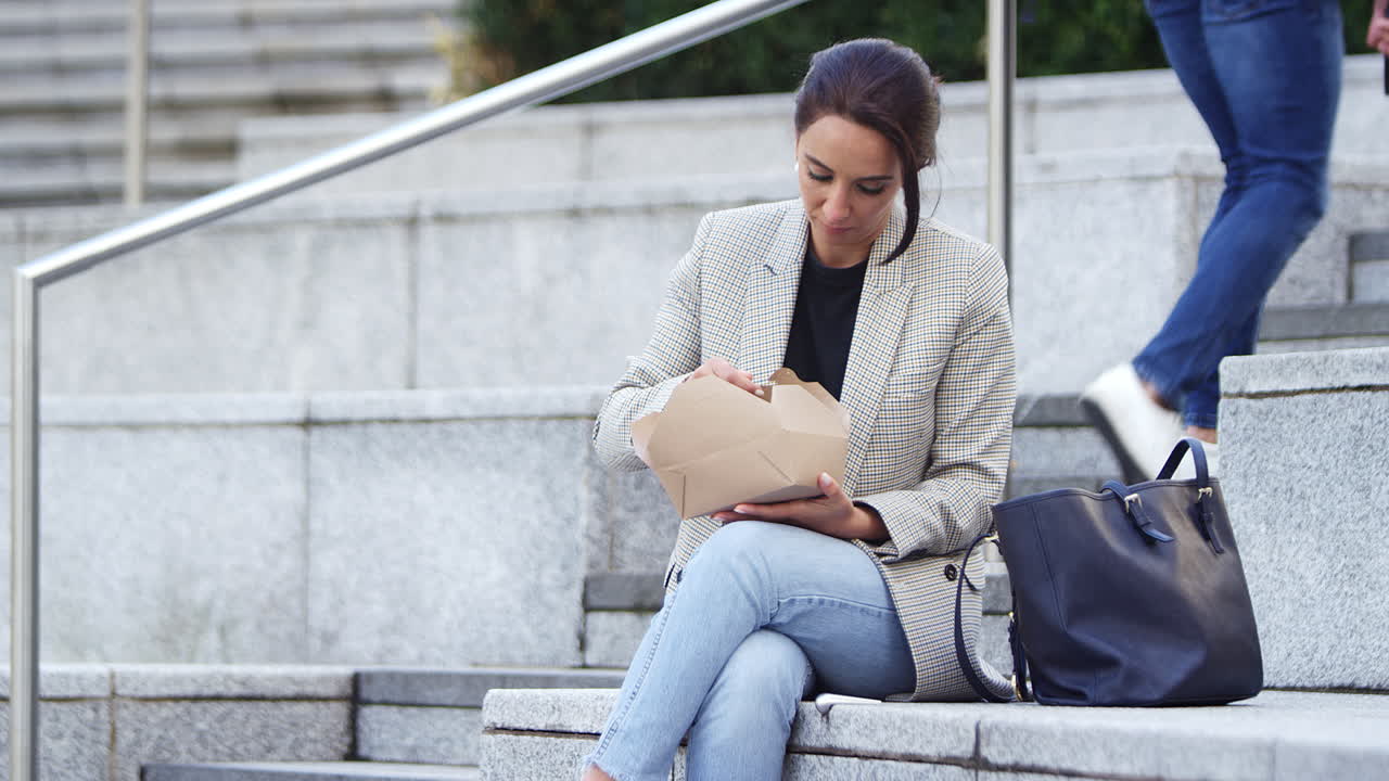 mujer de negocios sentada afuera en la pausa de almuerzo comiendo comida para llevar de cartón reciclable