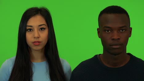 a young asian woman and a young black man look at the camera - closeup on the faces - green screen studio