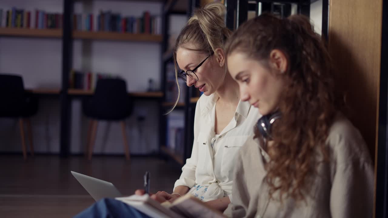 Female college students learning together and reading books in university library on the floor