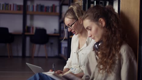 Estudiantes-Universitarias-Aprendiendo-Juntas-Y-Leyendo-Libros-En-La-Biblioteca-Universitaria-En-El-Suelo