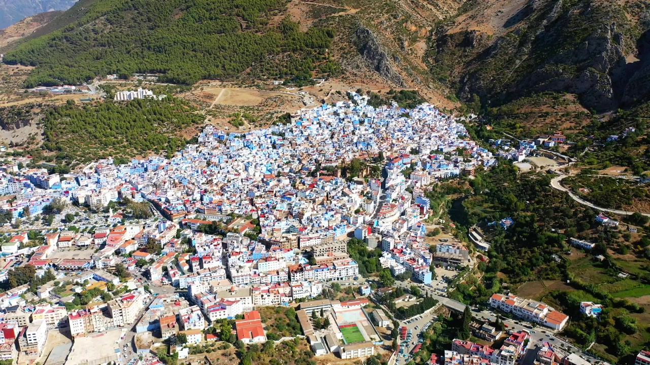 Ampia vista aerea con drone della medina blu di Chefchaouen, circondata dai Monti del Rif nel Marocco settentrionale. Paesaggio suggestivo di città di montagna ideale per progetti di viaggio e documentari