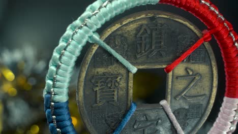 dreamy close-up shot of a chinese ancient traditional lucky coin, asian new year decoration, golden shiny blur background, square hole colorful strings culture holyday symbol, smooth pan left 4k video