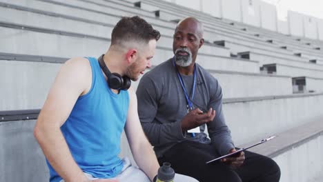 diverse male coach and athlete talking during night training session