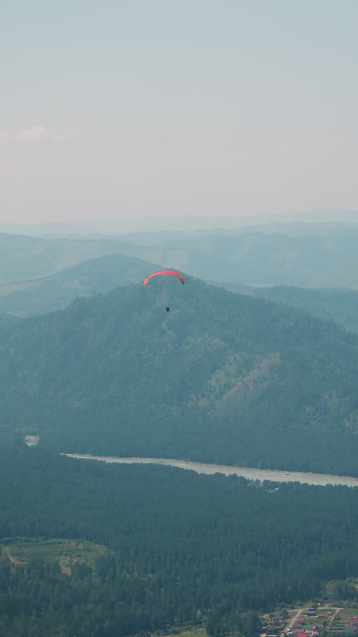 el parapente rojo brillante vuela sobre el gran valle verde con la ciudad del bosque y el río sinuoso en las viejas montañas pies en el día de verano cámara lenta