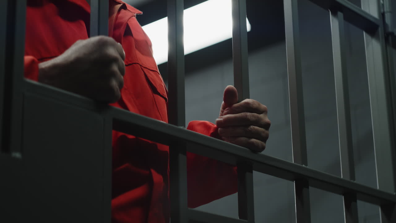 Prisoner in Orange Jumpsuit Behind Bars