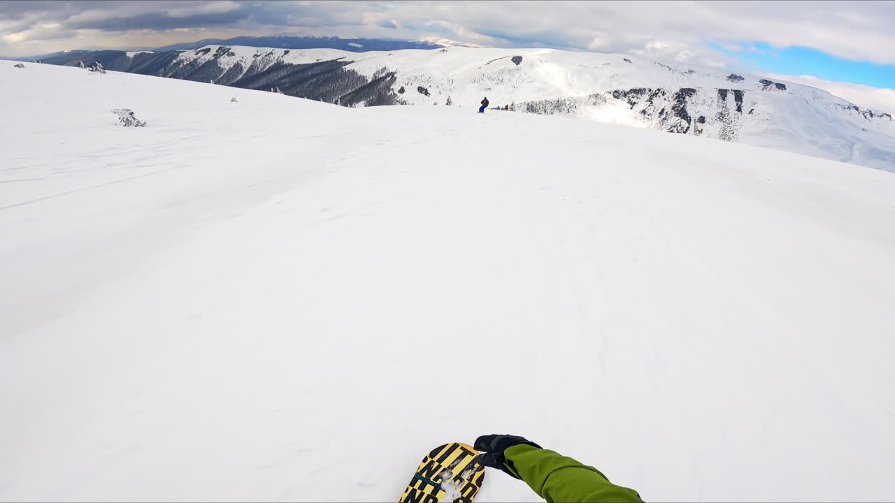 Pov: ride down the picturesque snowy slope of the mountain. Snowboarder taking video of the beautiful views.