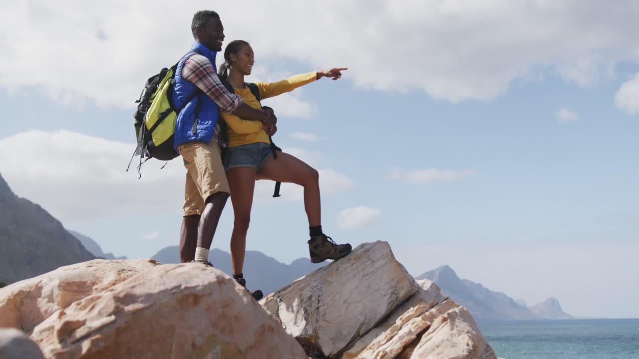 pareja afroamericana de pie en las rocas disfrutando de la vista mientras trekking