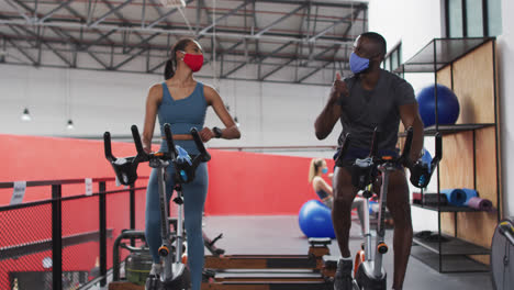 hombre y mujer con máscaras faciales tocando codos en el gimnasio