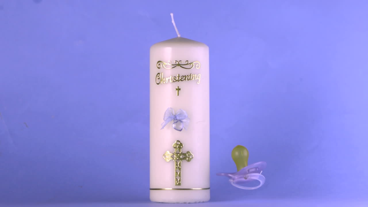 zapatos de bebé cayendo al lado de la vela de bautismo en fondo azul