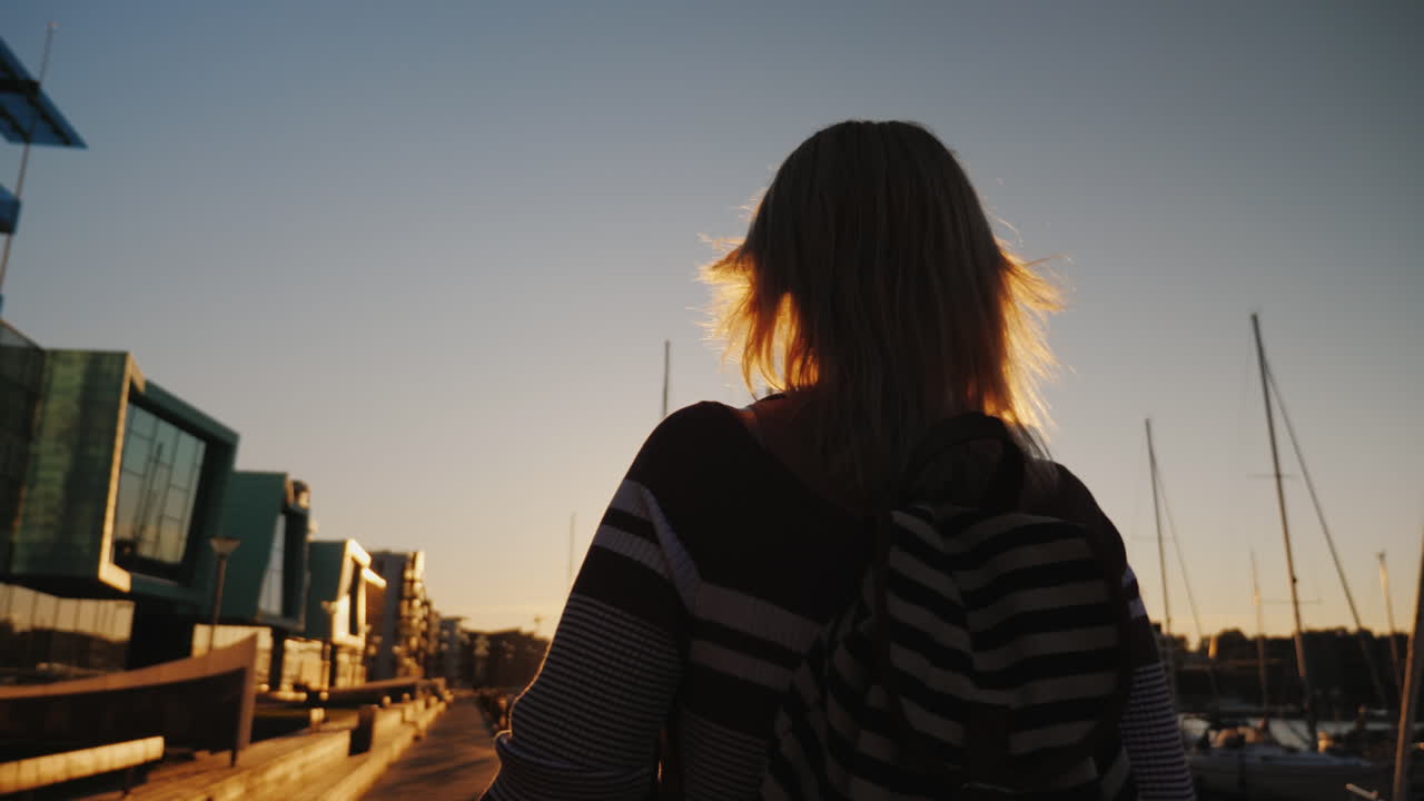 молодая женщина прогуливается по престижному району бергена возле пирса с яхтами.