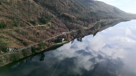 reflejos de nubes en un lago tranquilo con tráfico vial a orillas del lago y estructura parecida a un castillo en la costa