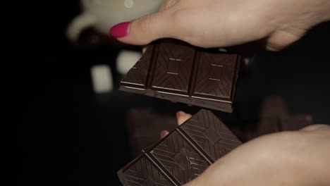 woman breaks black chocolate bar. close-up. slow motion