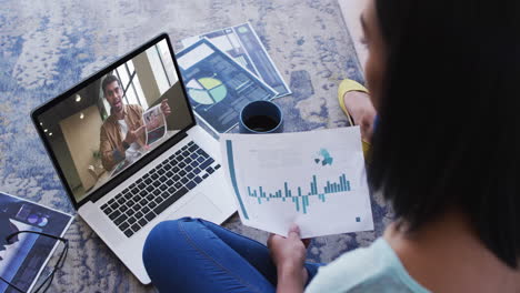 african american woman holding a document having a video call on laptop at home