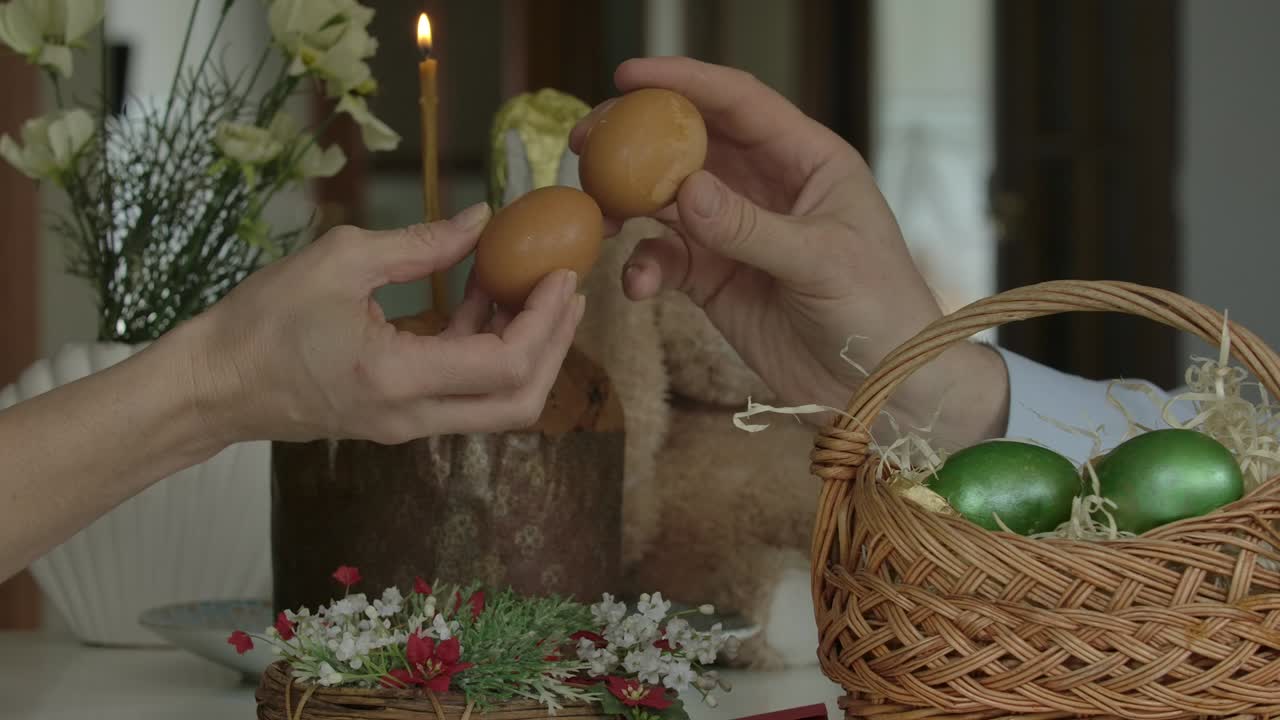 Male and female hands knocking eggs on Easter. Close-up side view of unrecognizable Caucasian man and woman performing tradition indoors. Traditional celebration, holy holiday, lifestyle.