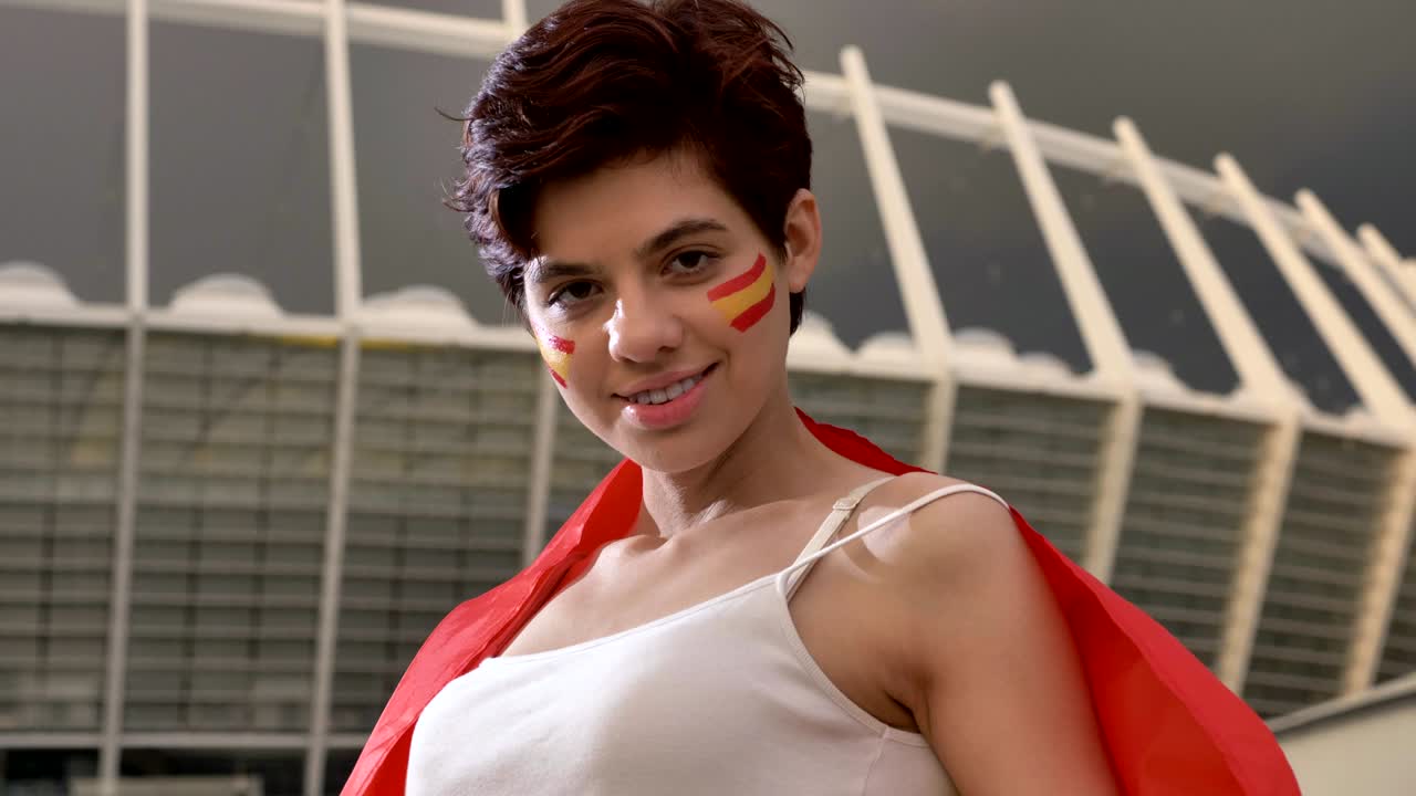 스페인에서 젊은 갈색 여자 축구 팬의 초상화, 카메라를보고, 미소 짓고, 웃고, 배경에 경기장 50fps