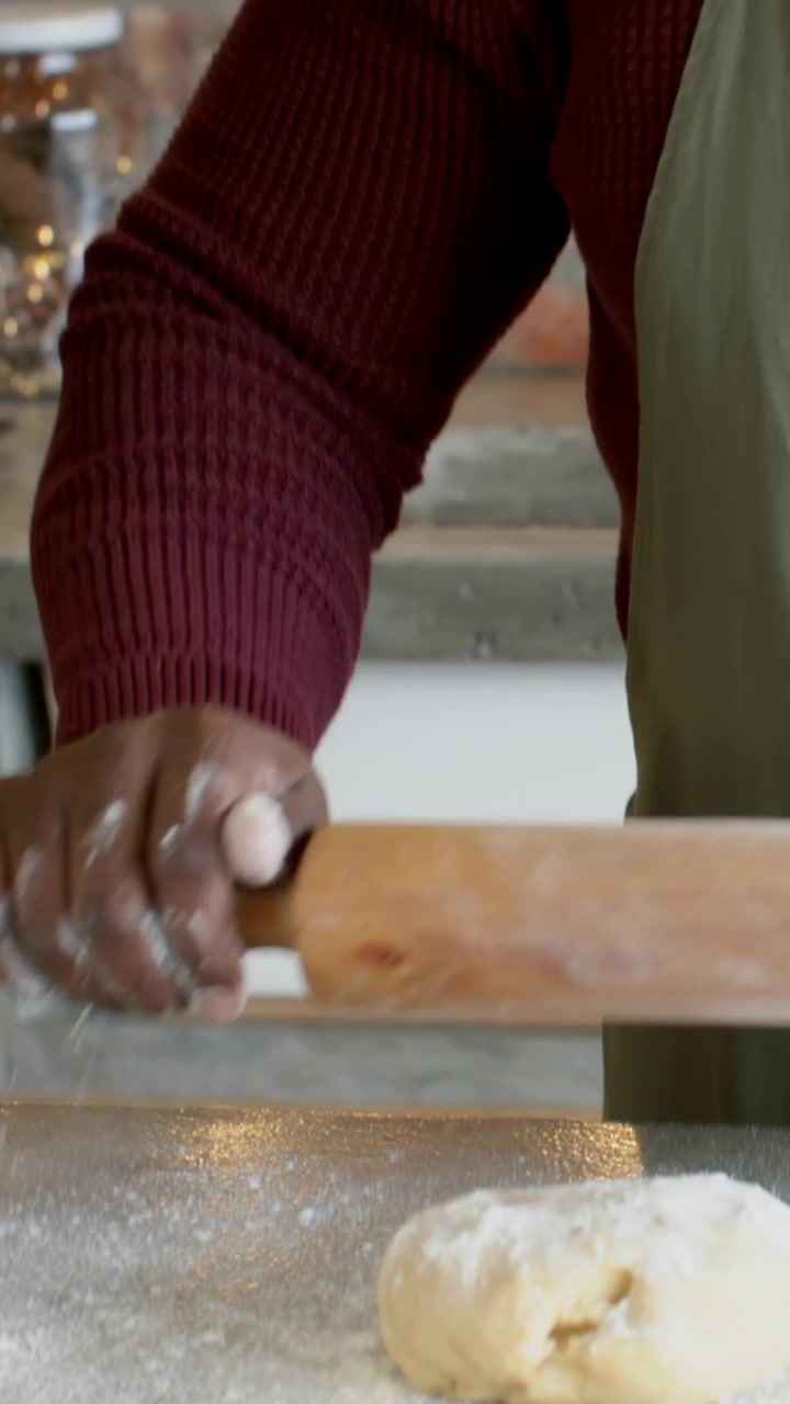 Vertical video: Dusting flour, baker apron rolling dough with pin at counter for treats, copy space