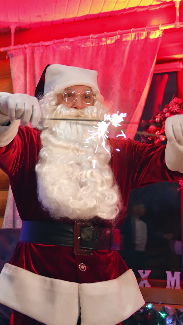 Funny Santa with Christmas lights dancing in the house. Real Santa Claus with white beard in glasses standing near beautiful Christmas tree. Santa looks at camera. Vertical video