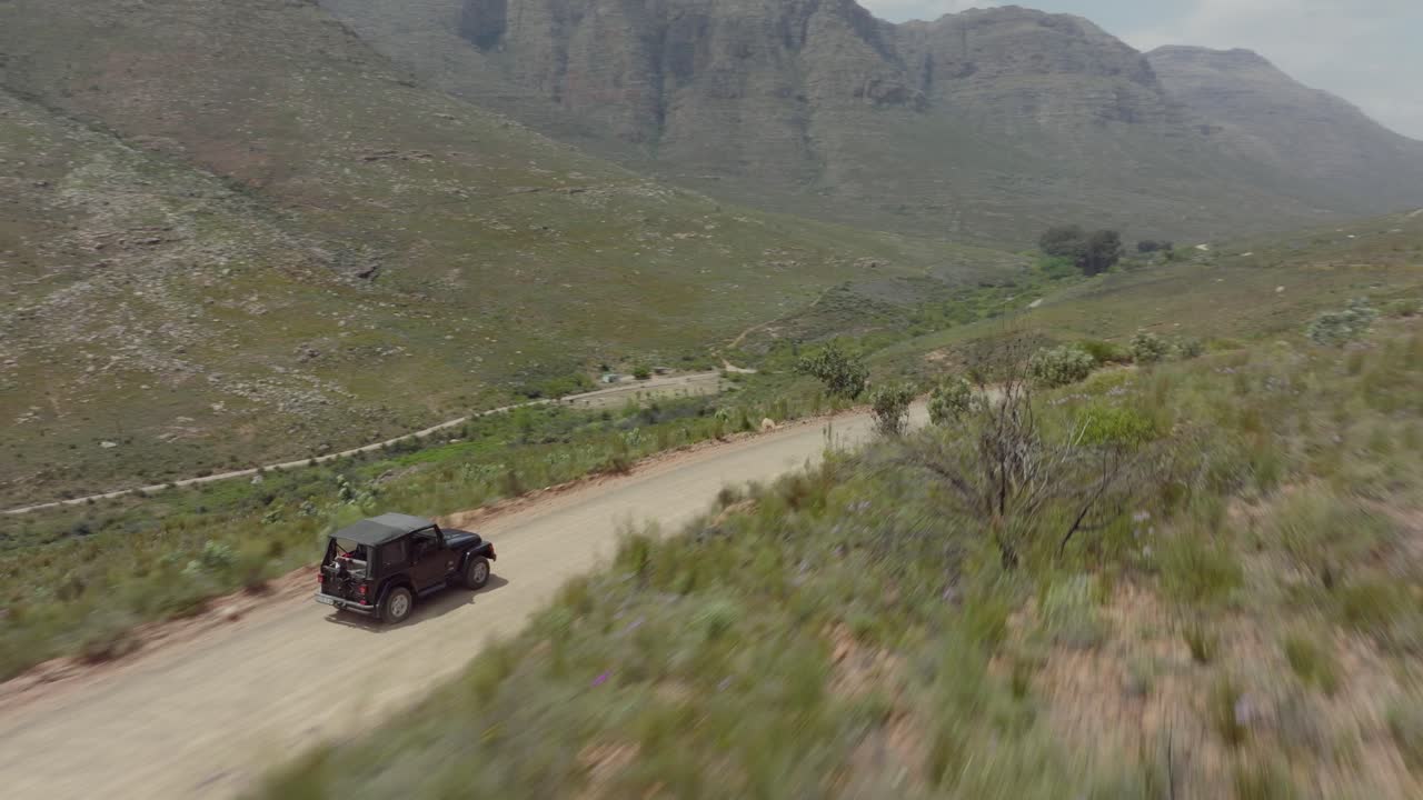 드론은 남아프리카 공화국의 세더버그 야생 지역의 바위 풍경의 도로 위에서 빠르게 날아가고 도로에서 운전하는 오프로드 차량을 따라갑니다.