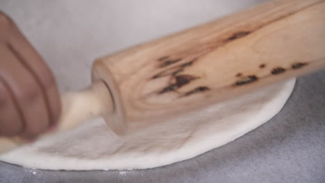 rolling out white dough with a wooden rolling pin, preparing dough for baking, close up