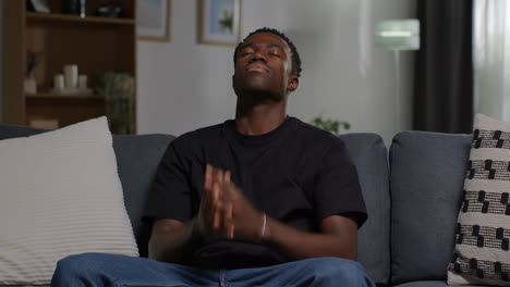 unhappy and depressed young man sitting on sofa at home closing eyes and shaking head