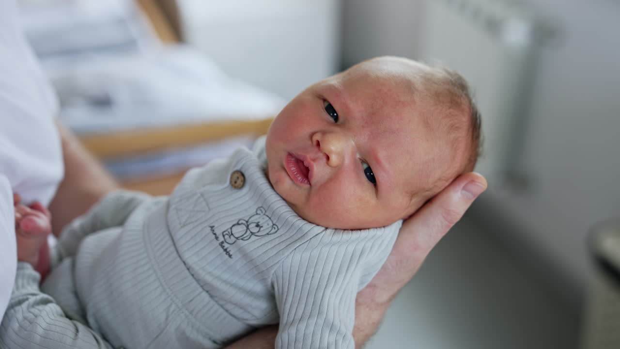 Adorable tiny infant lying on a dad's hand. Newborn closes his eyes slowly falling asleep. Close up.