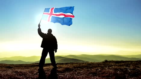 exitoso hombre silueta ganador agitando la bandera de islandia en la parte superior del pico de la montaña. fondo de bucle cinemagraph