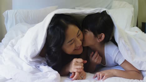 mother and daughter relaxing under blanket in bedroom 4k