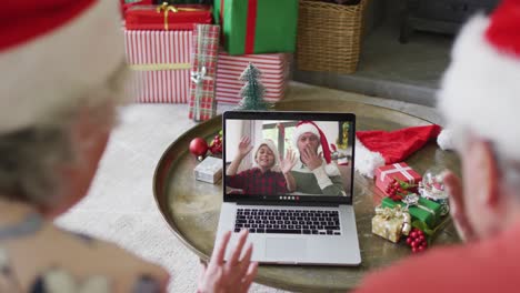 Senior-caucasian-couple-with-santa-hats-using-laptop-for-christmas-video-call-with-family-on-screen