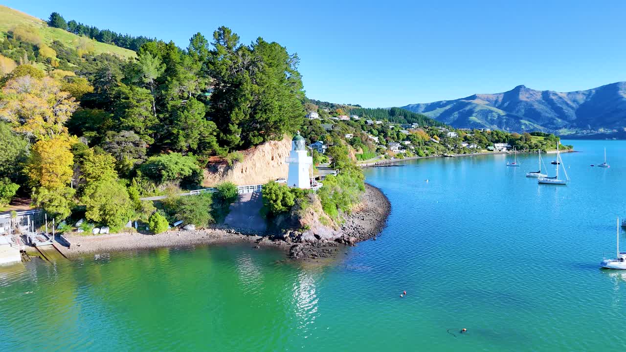 Aerial view of a lighthouse on a sunny day in Akaroa, New Zealand, showcasing vibrant landscapes and tranquil waters