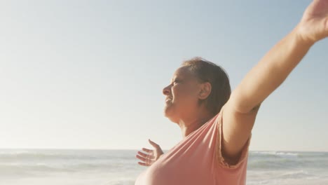 Smiling-senior-african-american-woman-with-arms-wide-on-sunny-beach