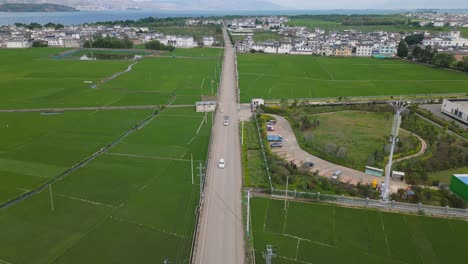 The-drone-footage-follows-some-cars-travelling-along-a-small-road-strip-surrounded-by-the-expansive-crop-fields-in-Dali,-Yunnan,-China