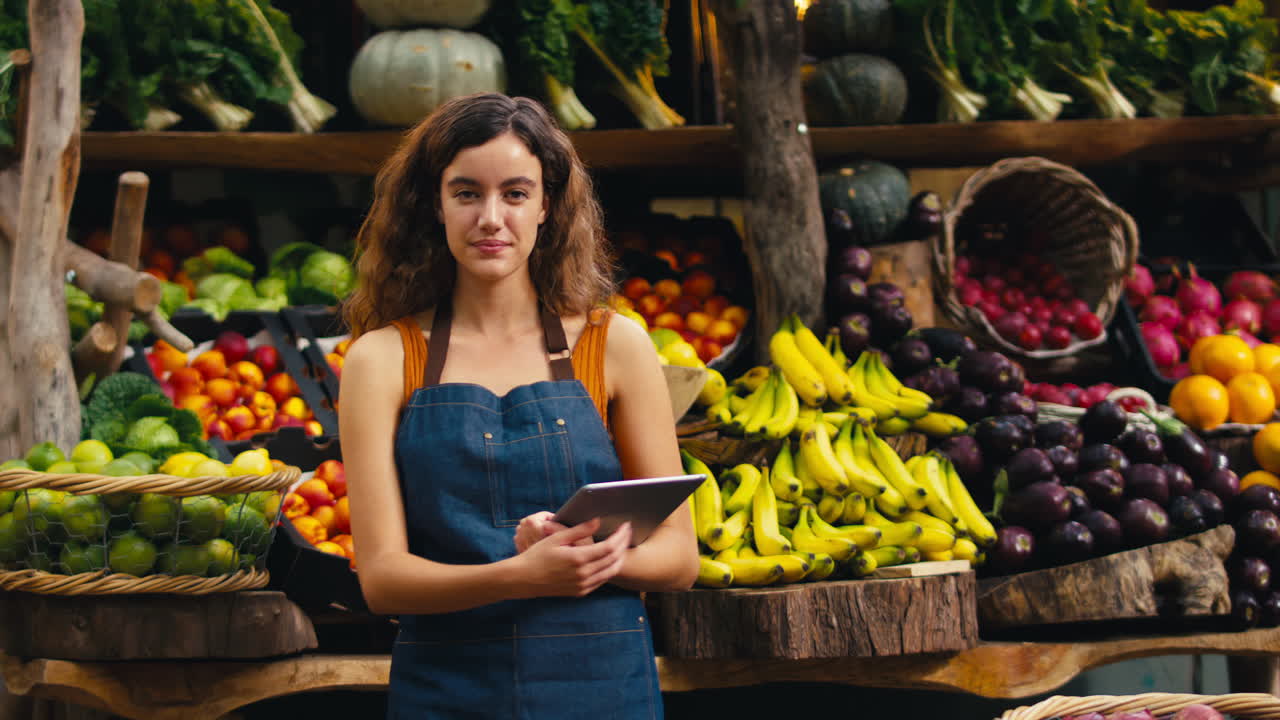 retrato de una mujer sonriente con una tableta digital trabajando en un puesto de frutas y verduras frescas en el mercado