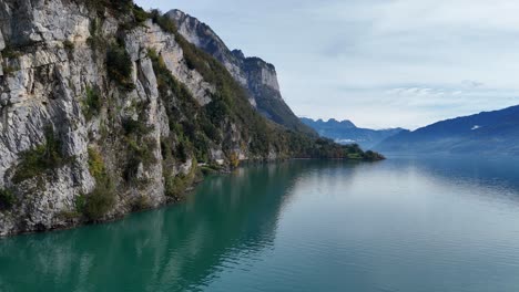 aerial panning shot showing steep cliff of mountains in switzerland at lake walen