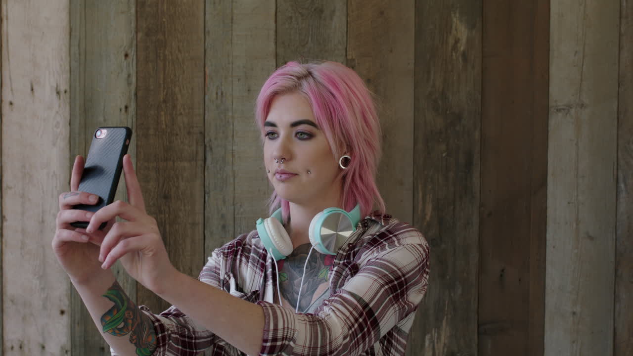 retrato de una joven punk de una mujer atractiva con un peinado rosa posando tomando una foto selfie utilizando la tecnología de la cámara del teléfono inteligente