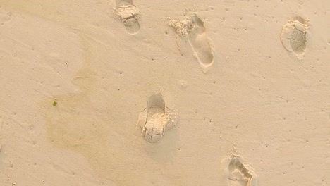 Vogelperspektive-Von-Oben-Nach-Unten-Nach-Verschiedenen-Aufgedruckten-Nackten-Fußspuren-Und-Schuhsohlen-An-Einem-Unberührten-Strand