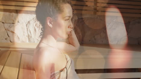 animación de velas y puntos de luz sobre mujer biracial relajándose en la sauna