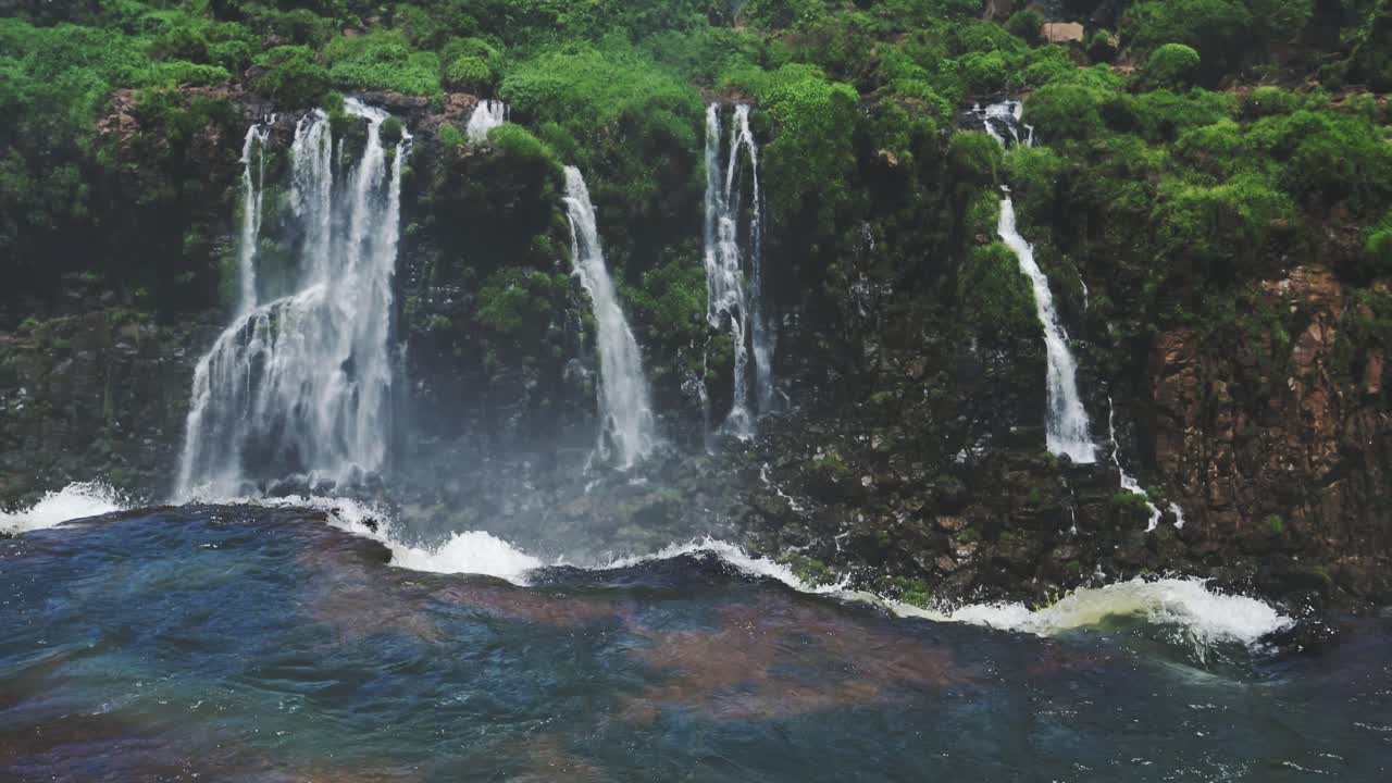 las cataratas de iguazu caen lentamente. el arroyo cae de un enorme acantilado en la distante selva. paisaje de selva tropical, alta vegetación que rodea una hermosa cascada clara que cae del borde de un acantilado alto en brasil.