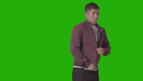 three quarter length portrait of cold shivering casually dressed young man doing up coat against green screen