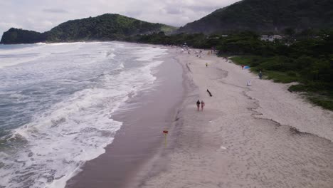 drone fying over the shore while people walks near the waves