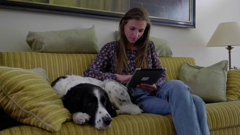 young woman sits reading table on couch with pet dog