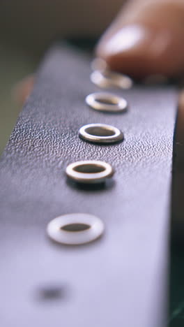 cu: professional tailor puts silver eyelets into fashionable black leather belt in workshop extreme close view
