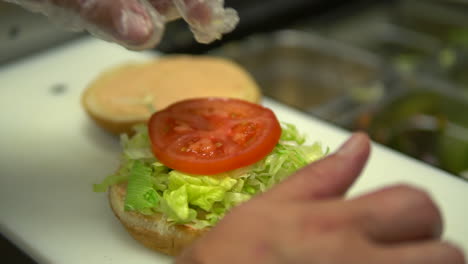 adding tomato slice to hamburger bun with lettuce, slow motion closeup