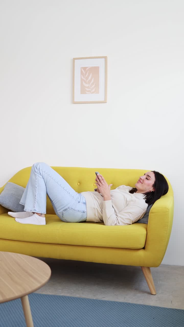 Giovane donna che si rilassa su un divano giallo e usa lo smartphone