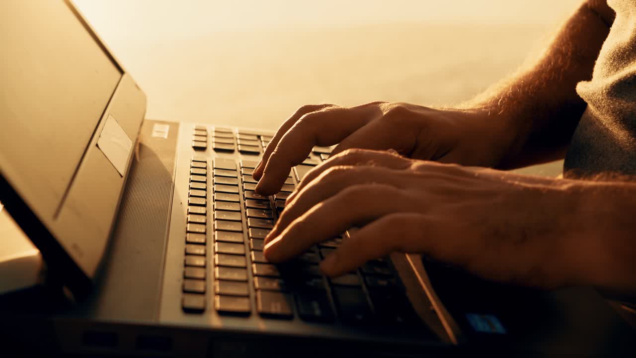Close-up young man working on laptop outdoors. Beautiful summer sunset by the river