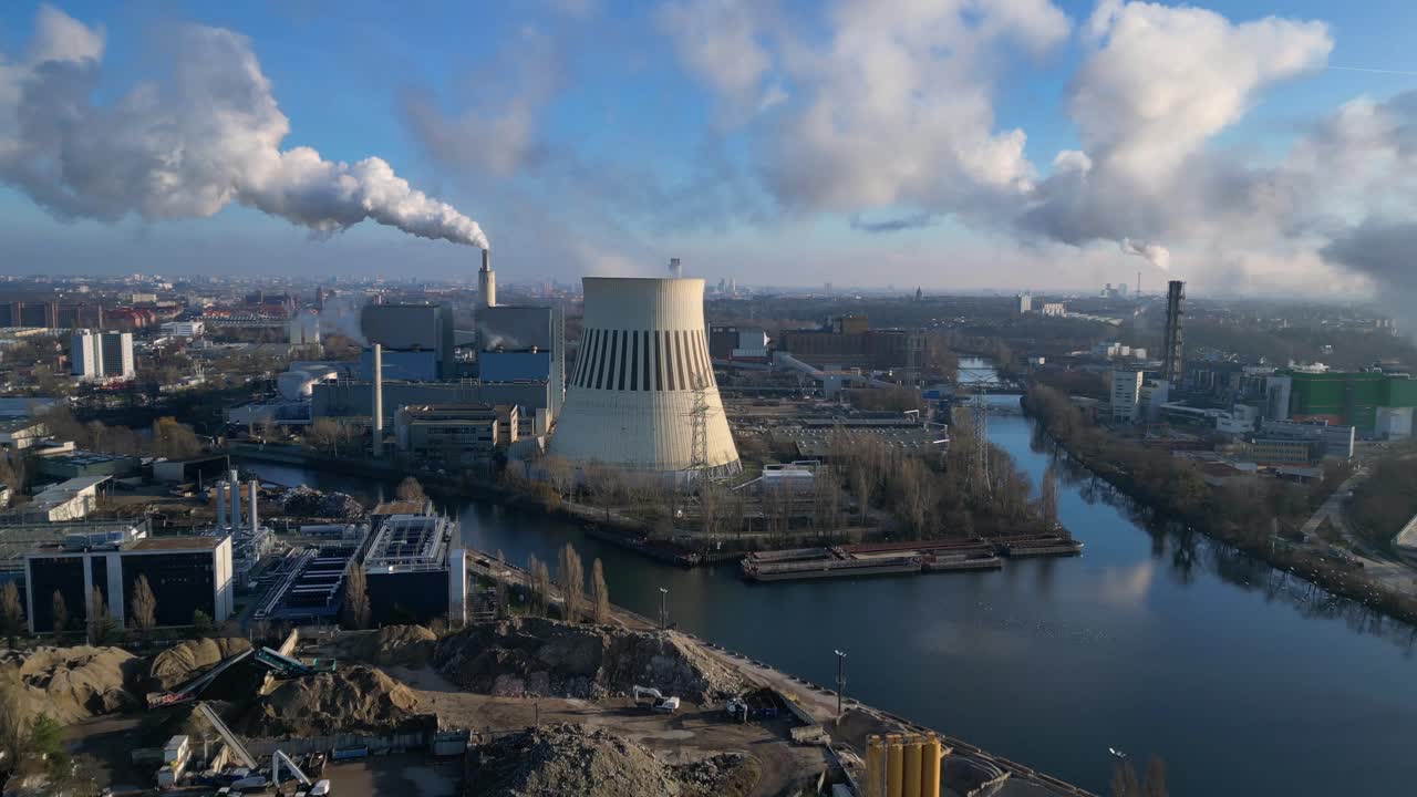 power plant emitting steam from its cooling tower, situated by a river and overlooking the cityscape. Fantastic aerial view flight fly reverse drone