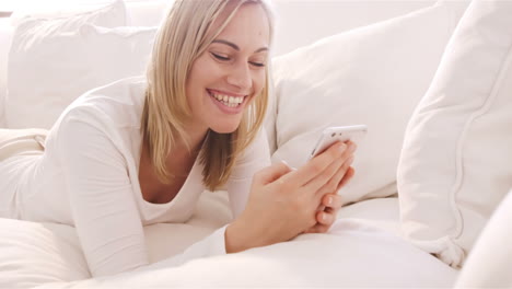 Mujer-Rubia-Tumbada-En-Un-Sofá-Usando-Su-Teléfono-Inteligente-Y-Sonriendo