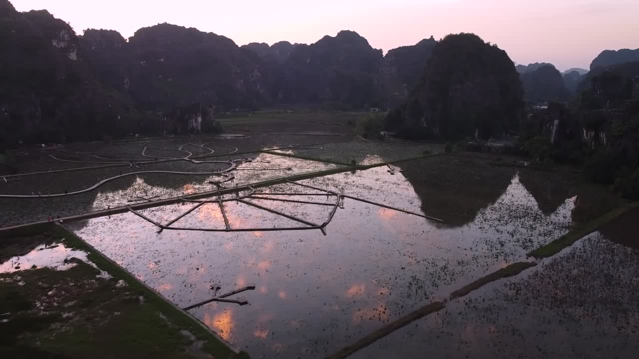 Máy bay không người lái bay qua con dê trắng và em bé đứng trên rìa, hé lộ những ngọn núi đá vôi karst rộng lớn và thung lũng với những đám mây phản chiếu trên mặt nước, lúc hoàng hôn