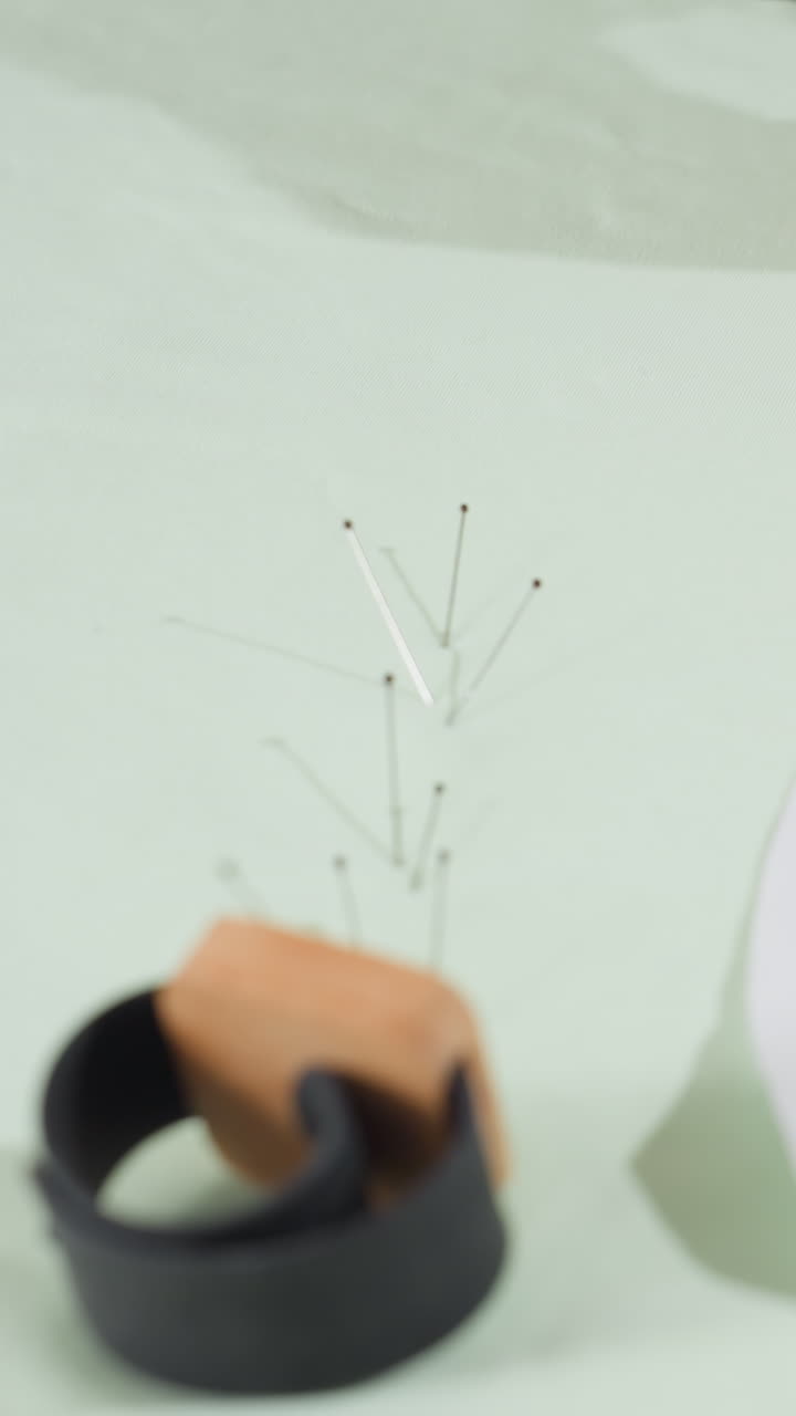 closeup pin mapping on fabric using wooden holder, hand inserting clustered pins into pale green textile to mark pattern points, compact organizer ring beside pins, steady motion, workshop tutorial